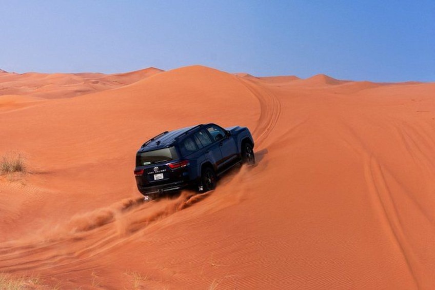 A blue SUV driving on a sandy desert landscape. 1
