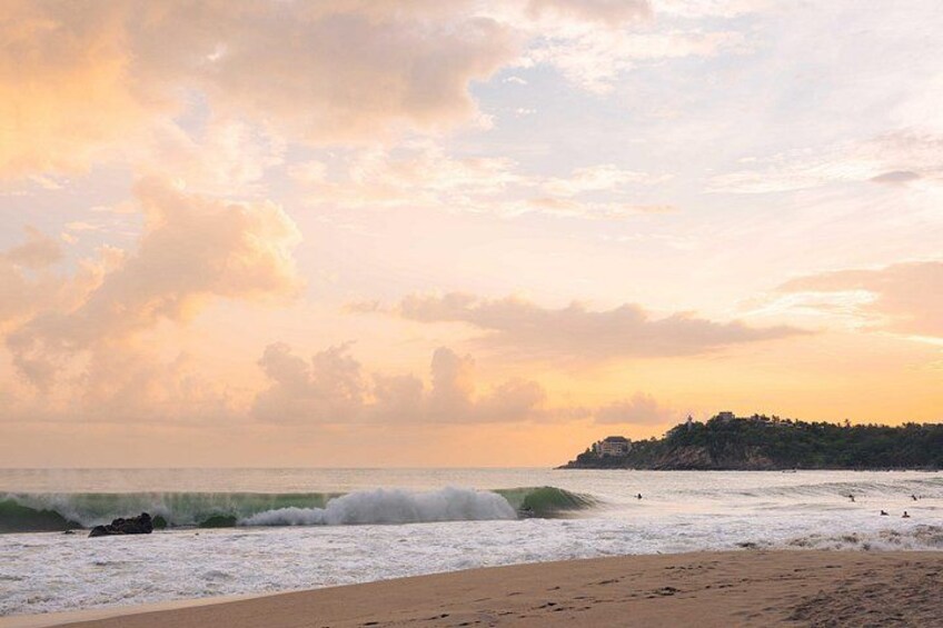 Una playa con olas, un litoral rocoso a lo lejos y un cielo al atardecer. 2