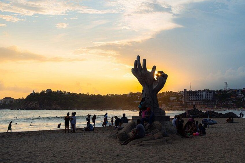 Una playa con gente, una gran escultura y un atardecer. 1