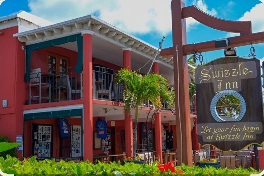 A Swizzle Inn building with a sign, palm trees, and a clear sky. 4