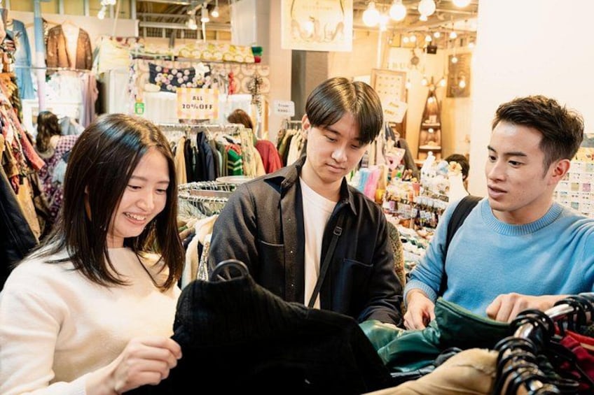 A clothing store with racks of clothes and a sale sign. 1