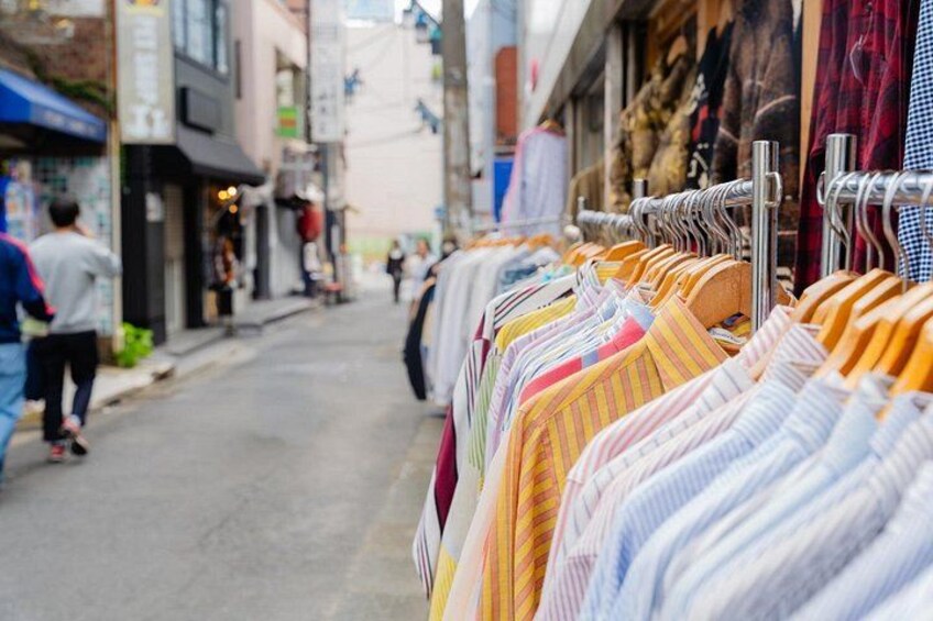 A street with clothing racks on the right and pedestrians on the left. 2