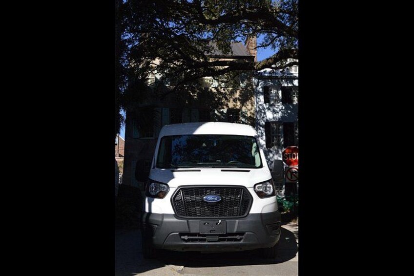 A white vehicle parked on a street with trees and a building in the background. 2