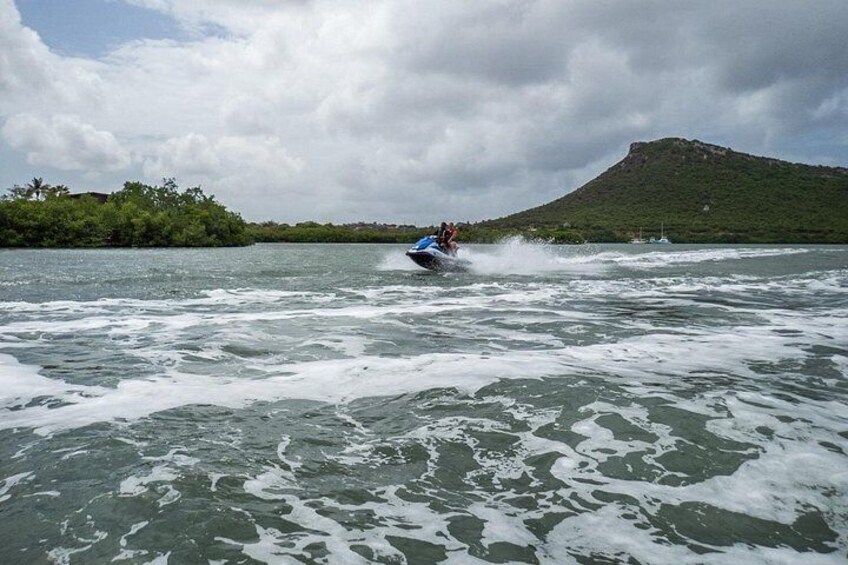 Een jetski op een rivier met golven, een groene heuvel op de achtergrond en een bewolkte lucht. 3