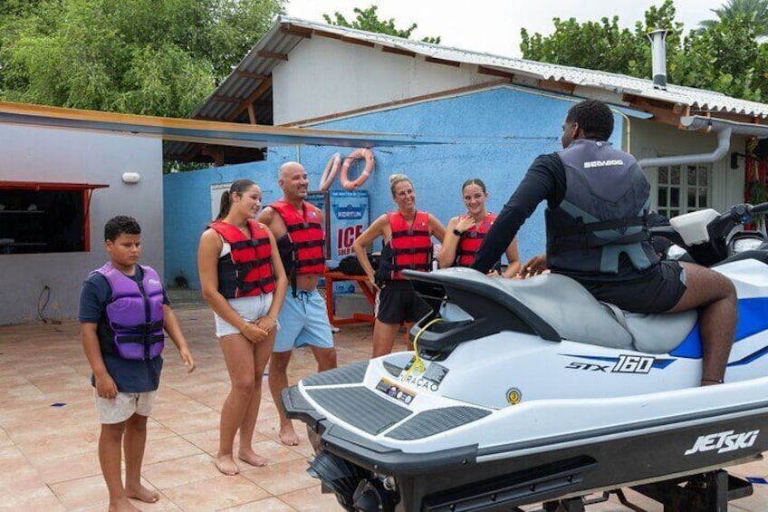 Un jet ski, des personnes portant des gilets de sauvetage et un bâtiment avec un mur bleu et une enseigne. 5
