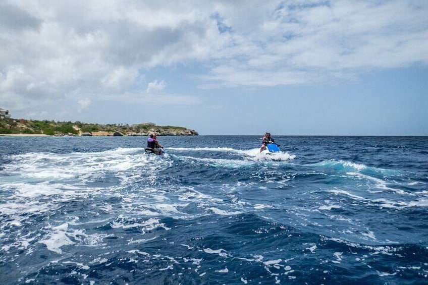 Deux personnes font du wakeboard sur une mer agitée, avec une côte visible à l’arrière-plan. 3