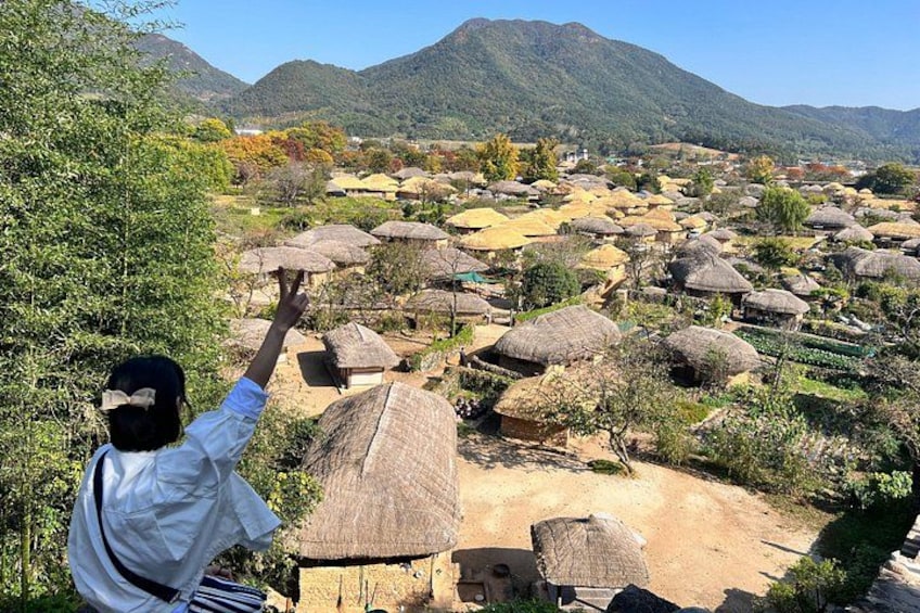 A rural landscape with thatched-roof huts, a person pointing towards the horizon, and mountains in the background. 1