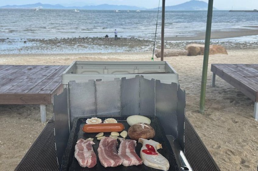 A grill with various meats and vegetables on a beach. 4