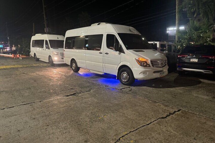 Two white vans parked on a wet road at night with blue underglow lights. 4
