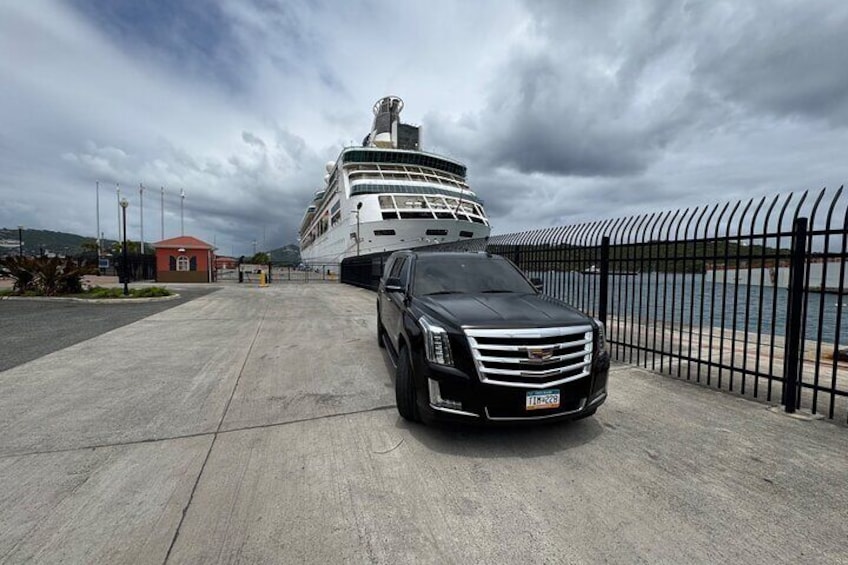 A cruise ship docked at a port with a black car parked in front. 2