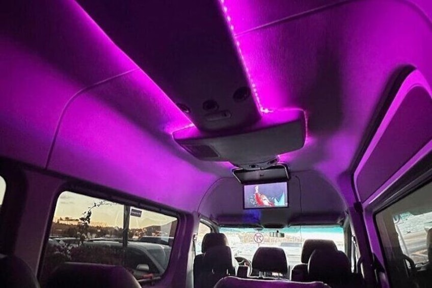 The interior of a vehicle with purple ambient lighting and a small screen mounted on the ceiling. 3