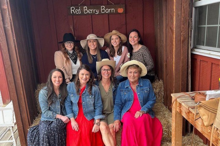 Un gruppo di persone seduto in una stalla con fieno sul pavimento e un cartello con la scritta 'Red Berry Barn'. 4