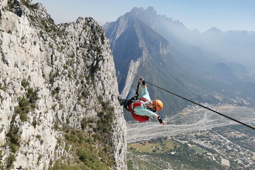 Eine Person seilt sich an einem steilen Felsen ab, umgeben von gebirgiger Landschaft und einem Tal darunter. 1