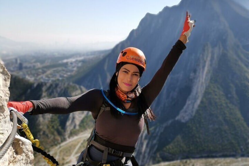 Eine Person seilt sich einen Berg hinab, mit Helm und Klettergurt, vor einer bergigen Landschaft. 5