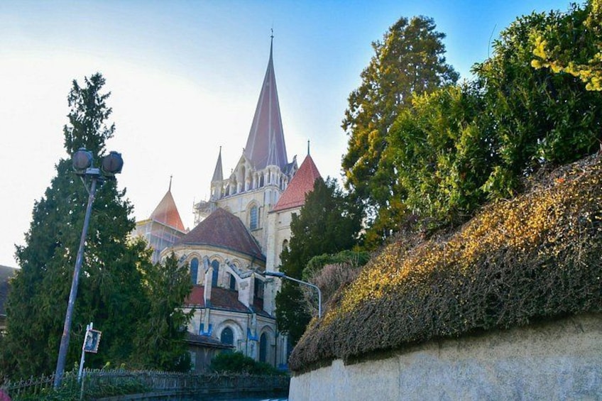 Eine historische Kirche mit einem spitz zulaufenden Turm, umgeben von üppiger Vegetation und einer Steinmauer. 3
