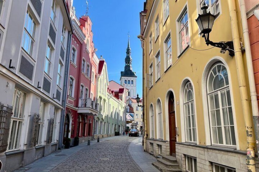 Eine Kopfsteinpflasterstraße gesäumt von farbenfrohen Gebäuden, einem Kirchturm und einer Straßenlaterne. 3