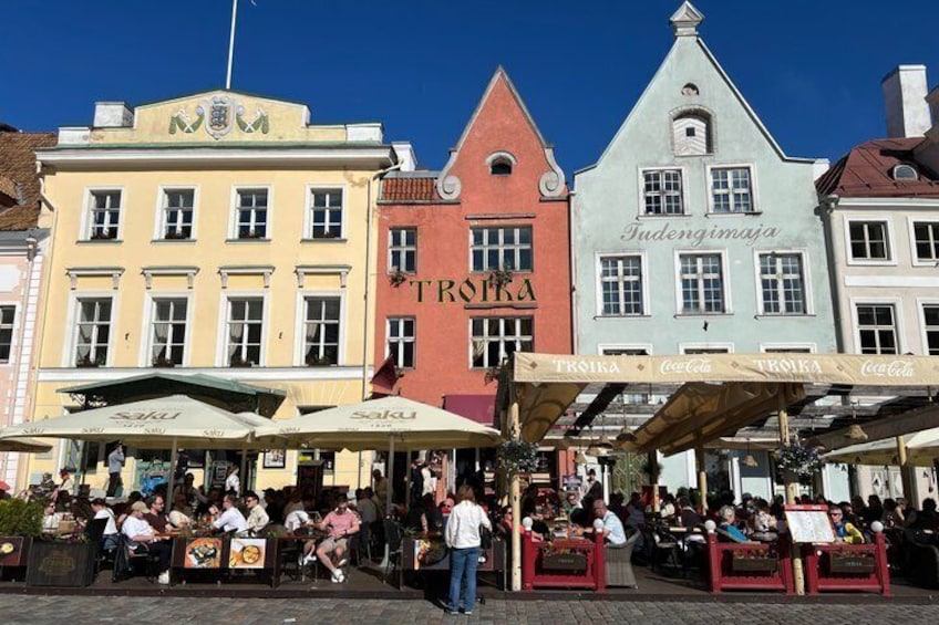 Eine Straße mit bunten Gebäuden, Außenbestuhlung und Menschen beim Essen. 5