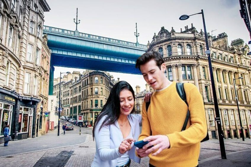 A couple standing on a city street with historic buildings and a blue bridge in the background. 1