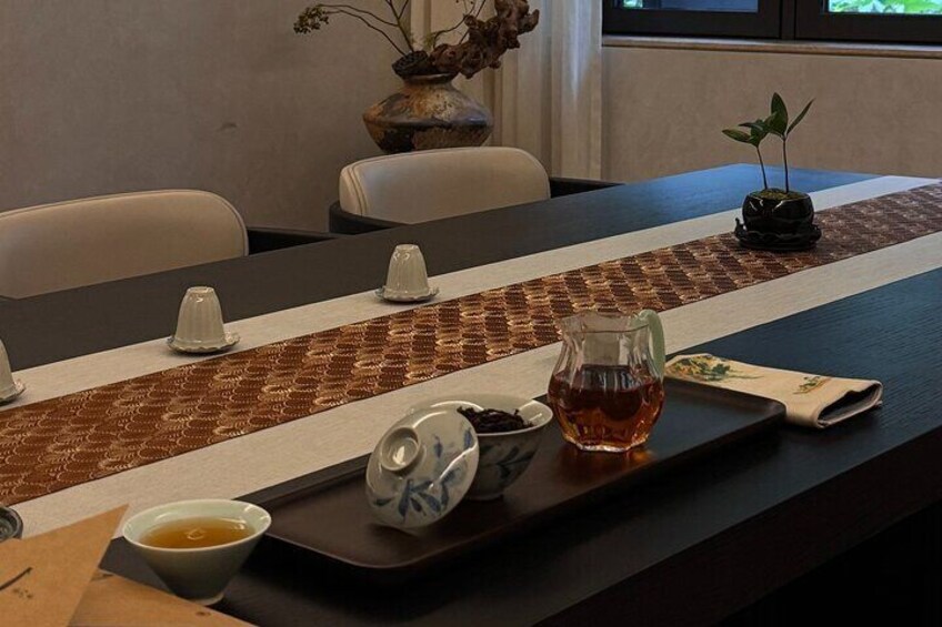 Ein Esstisch mit Untertasse, eine Teekanne, eine Suppenschüssel und einer kleinen Pflanze. 1