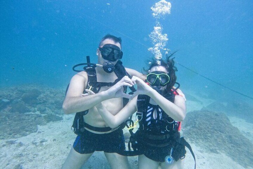 Two scuba divers underwater, one making a heart shape with their hands. 1