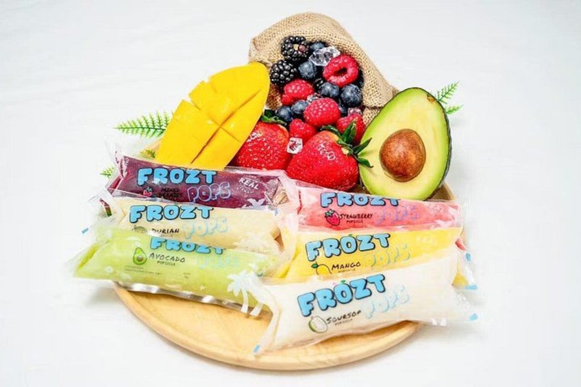 A wooden board with various frozen fruit bars and fresh fruits like strawberries, blueberries, mango, and avocado. 5