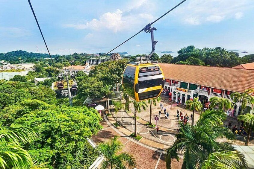 A cable car system with a cable car suspended between two towers, a building with a red roof, and lush green trees. 2