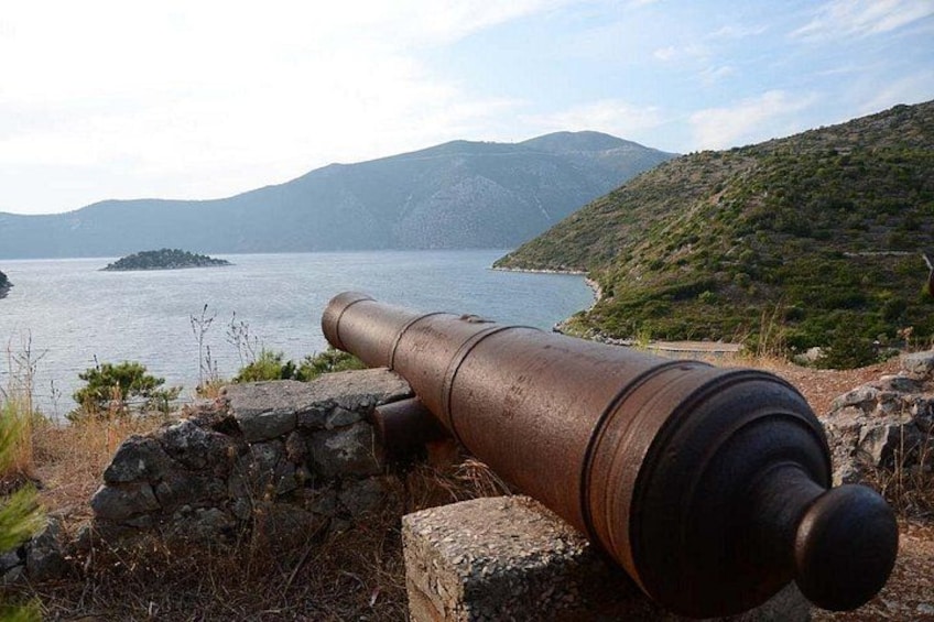 Un canon est installé sur un promontoire rocheux, surplombant une étendue d’eau avec, au loin, une île et des collines. 2