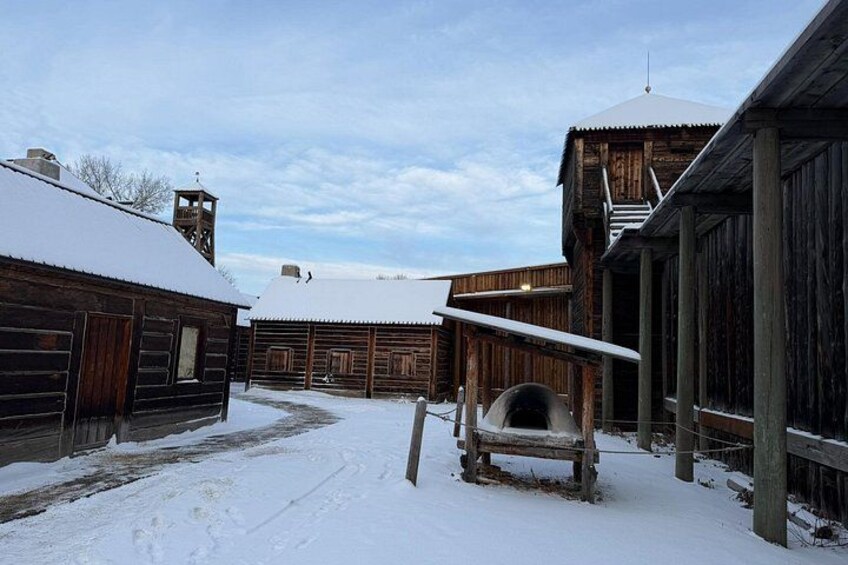 Et snødekt landskab med træbygninger, et kirketårn og sne på jorden. 3