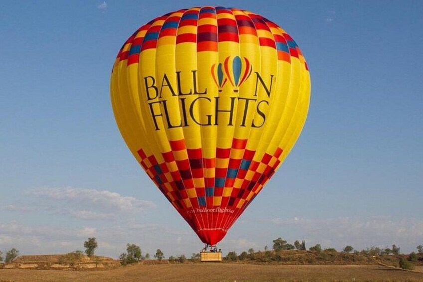 A hot air balloon with 'Balloon Flights' written on it, anchored on the ground with a clear sky in the background. 1