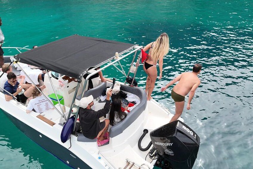 A boat with people on board, some standing and some seated, with a clear blue water background. 3