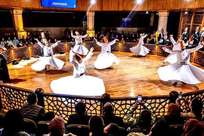 A group performing a traditional dance in a circular wooden stage with an audience seated around. 1