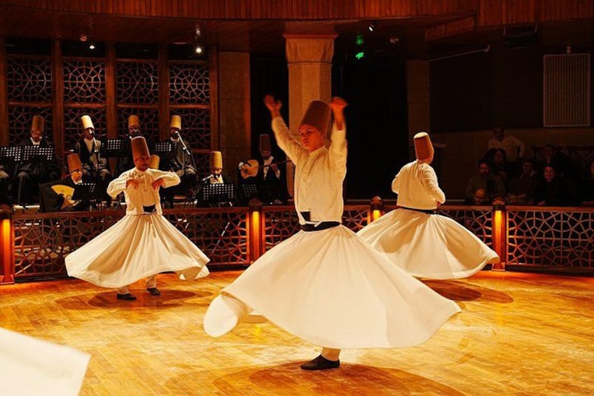 A dance performance with dancers in white dresses on a wooden floor, with an audience and musicians in the background. 2