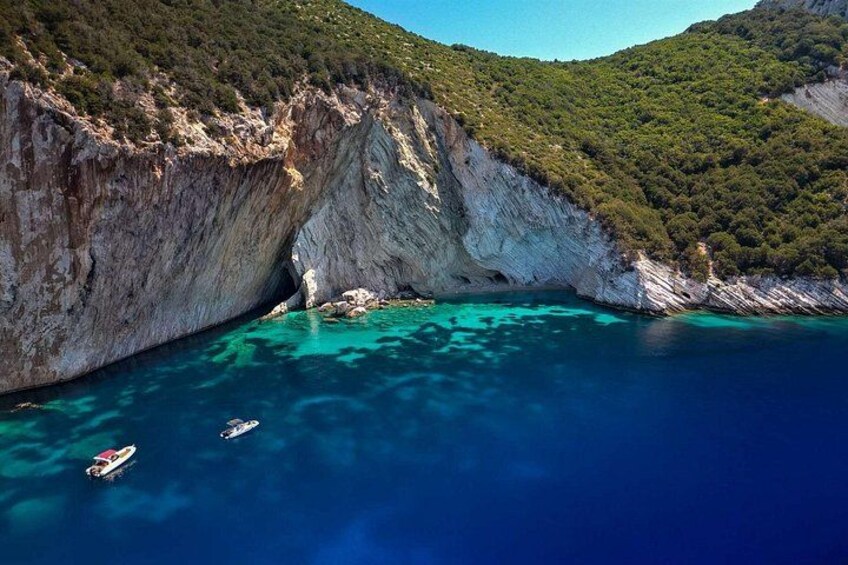 A coastal landscape with a cliff, clear turquoise water, and boats. 5