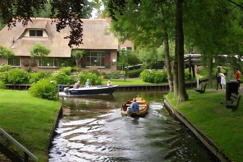 A narrow canal with boats, a grassy bank, and a building with a thatched roof. 2