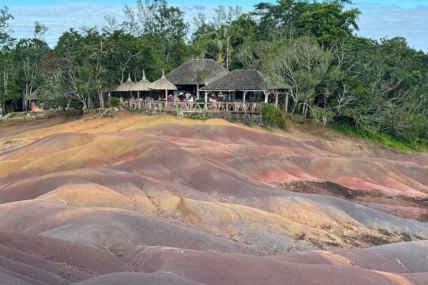 A beach with colorful sand formations, a wooden structure, and surrounding trees. 5