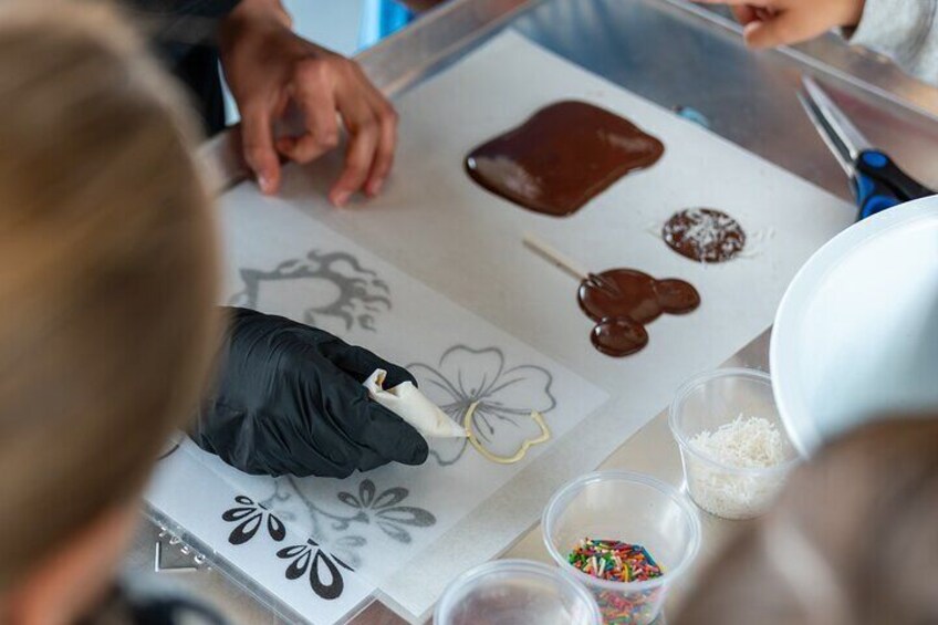 A person wearing black gloves applying chocolate to a white surface with a floral design. 1