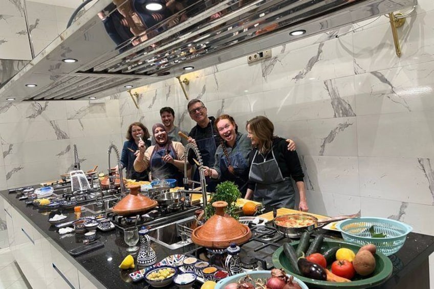Un groupe de personnes se trouve dans une cuisine, entouré de divers ustensiles de cuisine, de casseroles et de légumes frais disposés sur le plan de travail. 1