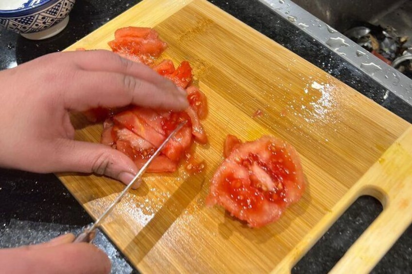 Une personne qui tranche une tomate sur une planche à découper en bois. 2