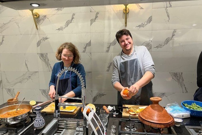 Deux personnes préparent un repas dans une cuisine aux murs de marbre, équipée d’une cuisinière et de divers ustensiles de cuisine. 5