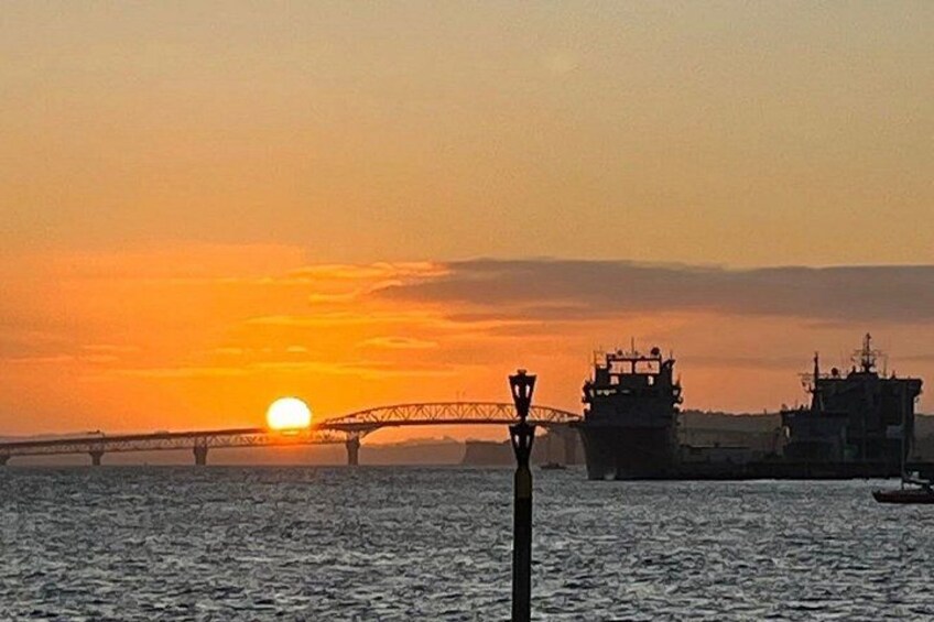 Ein Sonnenuntergang über einem Gewässer mit einer Brücke und Industriegebäuden im Hintergrund. 4
