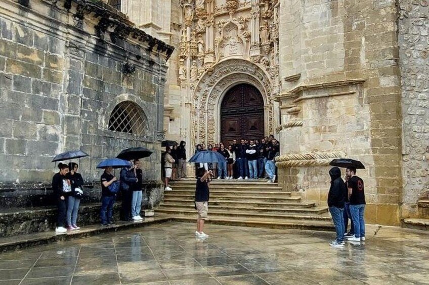 A historic building with ornate architecture, a group of people standing on steps, and individuals holding umbrellas. 3