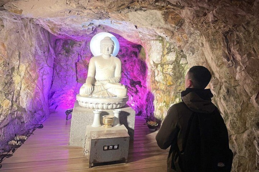 A seated Buddha statue in a cave with a person observing it. 2