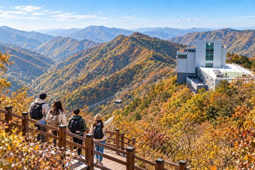 A group of people on a wooden observation deck overlooking a mountainous landscape with autumn foliage and a modern building. 1