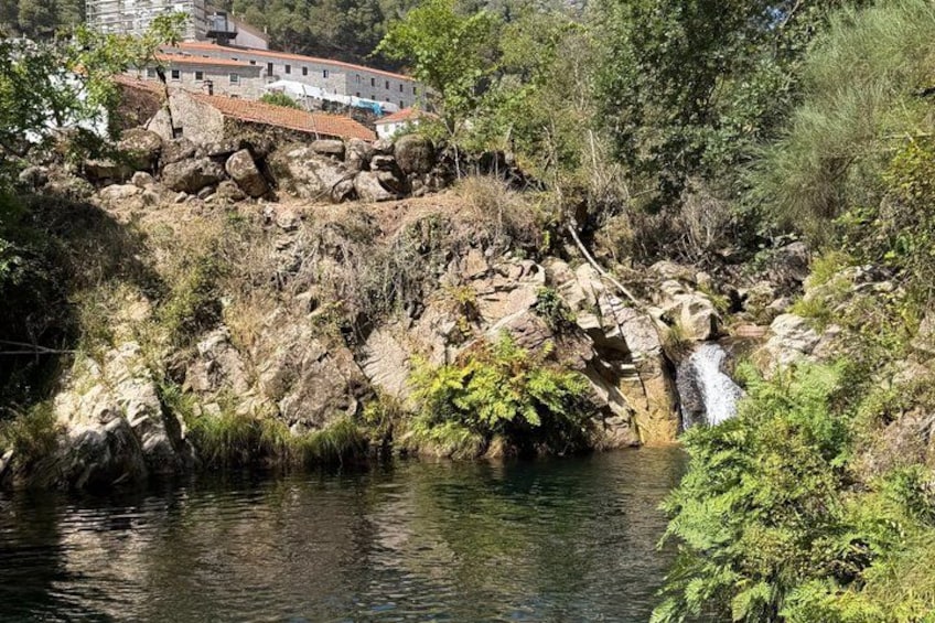 A rocky riverbank with a waterfall, lush greenery, and a building in the background. 3