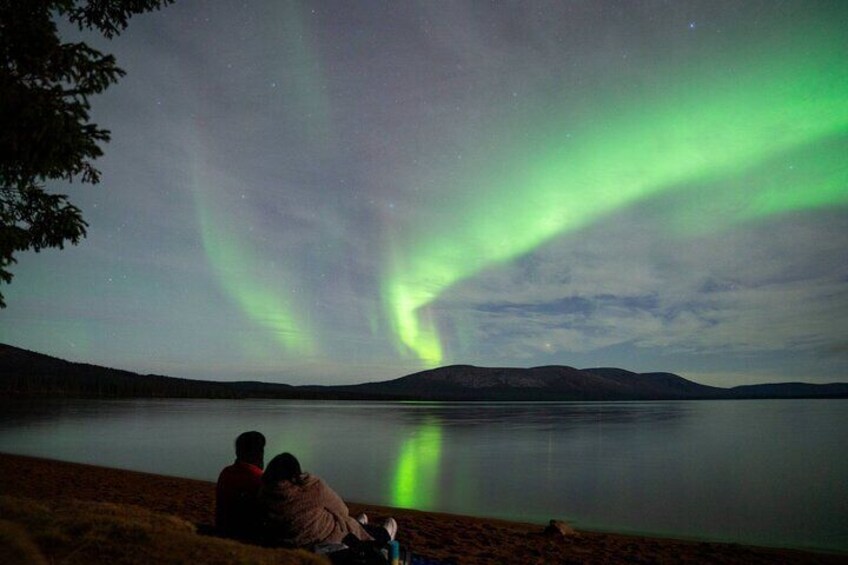 Two people sitting by a lake watching the Northern Lights. 2