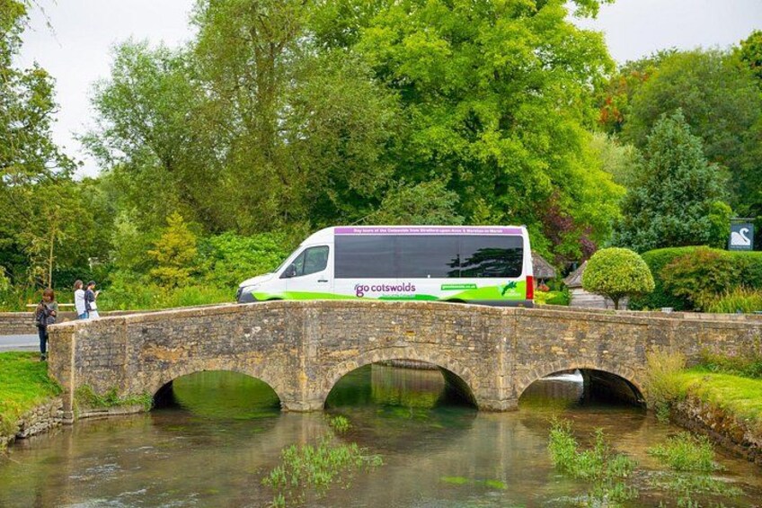 A green and white bus on a stone bridge over a river. 3