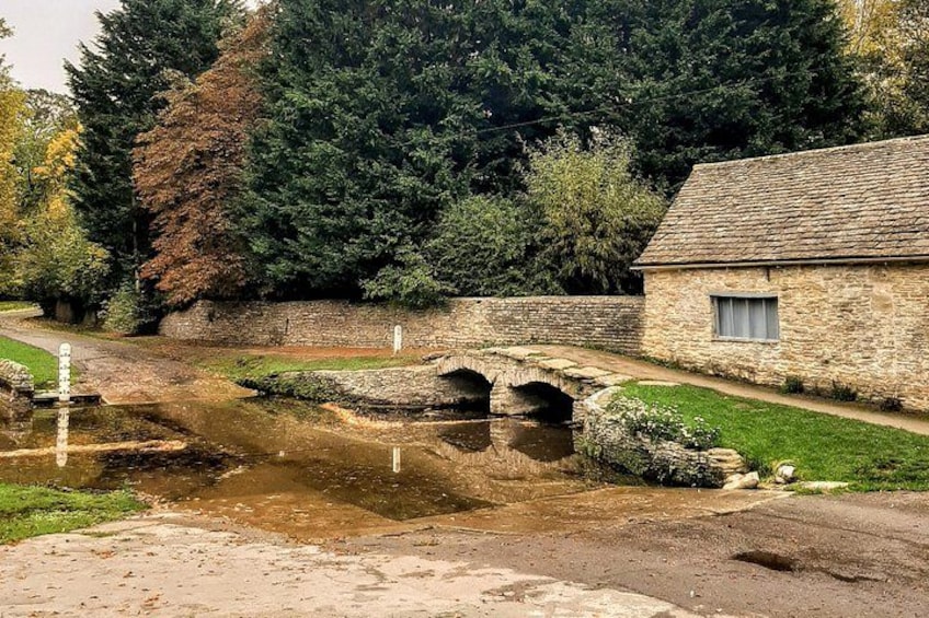 A stone bridge over a water channel, a stone building, and a forested area. 2