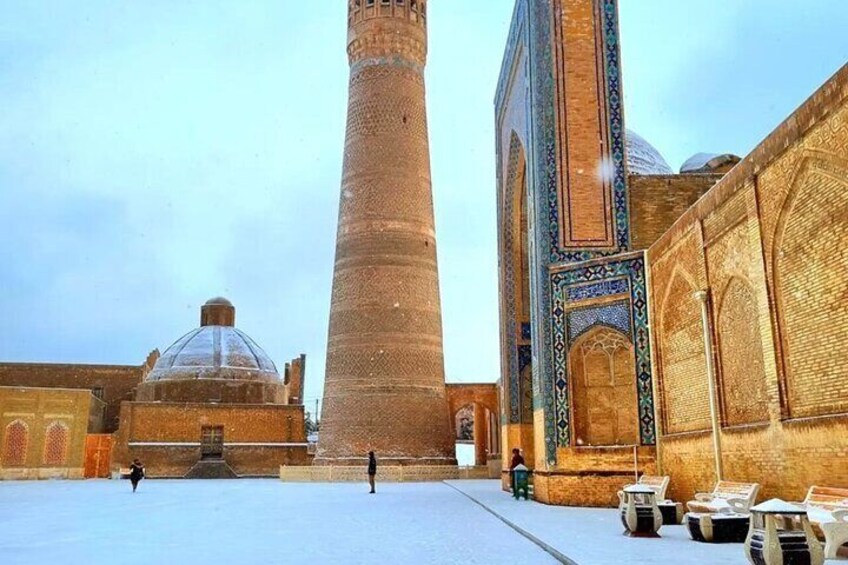 Ein mit Schnee bedeckter Innenhof mit einem hohen Ziegelminarett und einer Kuppelstruktur. 4