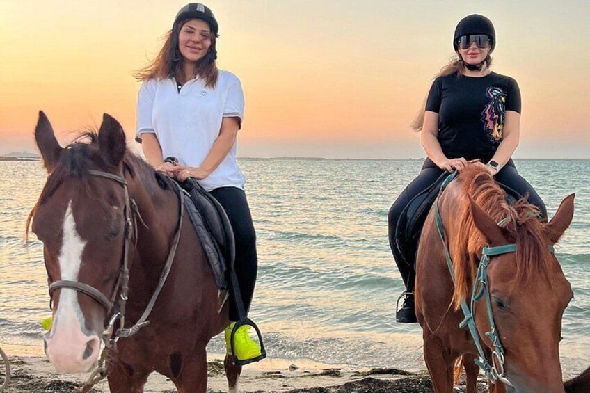 Two people riding horses on a beach with the ocean in the background. 4