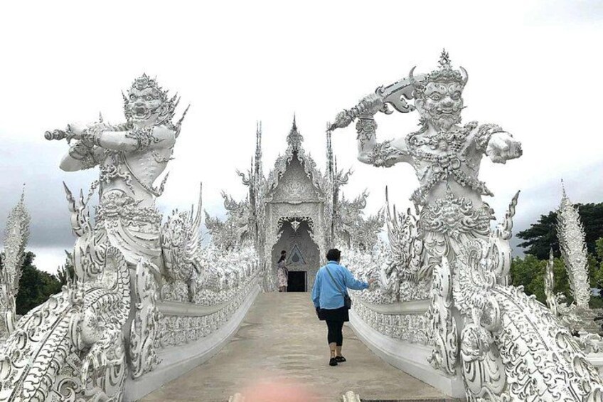 A person walking on a bridge with intricate white statues on either side. 1